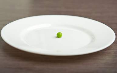 diet concept. one  pea on an empty white plate