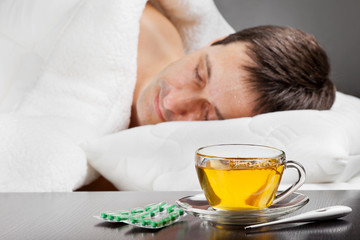Obraz na płótnie Canvas chory człowiek leży w łóżku z gorączką, filiżankę herbaty ziołowe, tabletki i