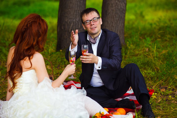bride redhead and groom wedding in green field sitting on picnic