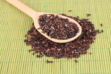 black rice  in wooden  spoon on bamboo mat