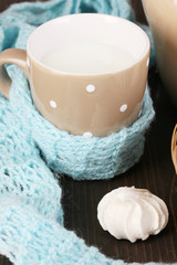 Pitcher and cup of milk with meringues on wooden table close-up