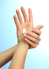 Beautiful woman hands with cream, on blue background