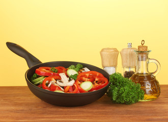 frying pan with vegetables on yellow background