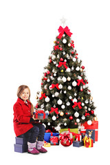 Happy girl sitting next to a christmas tree and holding present