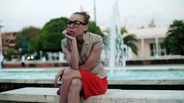 Young sad woman sitting along on a bench, outdoors, slow motion 
