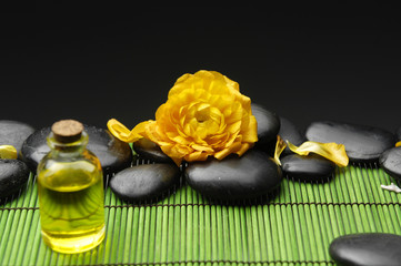 Fototapeta na wymiar butelka z olejem do masażu i pomarańczowy Ranunculus z kamieni na matę