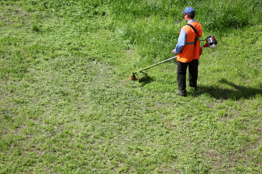 Man lawn-mower with chopper trimer moving grass at sunny summer