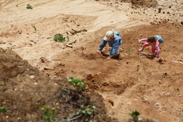 Top view of boy and girl with blue backpacks clamber on sand.