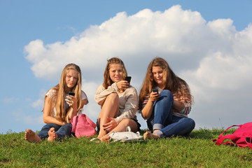 Naklejka na ściany i meble Three girls sit on grass with mobile phones