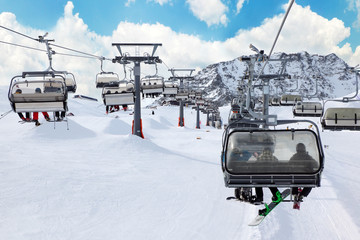 Obraz premium Ski chair-lift with skiers in snow-capped mountains in Austrian