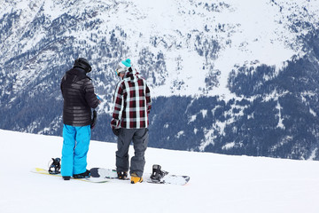 Two men with snowboards prepare for slope in snowy mountains.