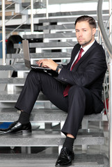 A businessman sitting on stairs smiling with a laptop computer