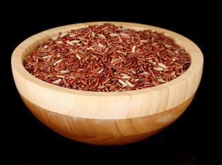 Red rice in wooden bowl isolated on black