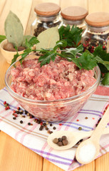 Bowl of raw ground meat with spices on wooden table