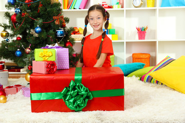 Little girl with large gift box near christmas tree