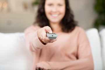 lächelnde frau mit fernbedienung auf dem sofa