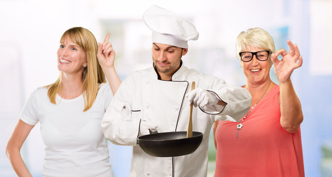 Male Chef Cooking Food While Happy Women Gesturing Behind