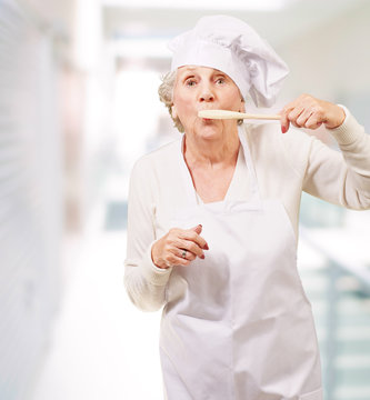 portrait of cook senior woman with wooden spoon on mouth indoor