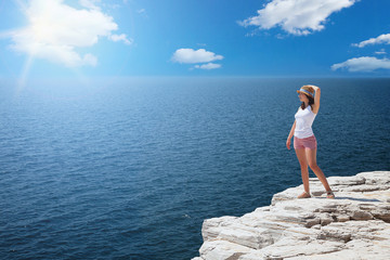 Young woman standing on cliff's edge and looking to a sea