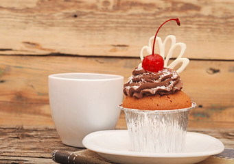 Cupcake with chocolate cream and cherry on old wooden background