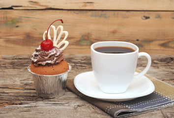 Cupcake with chocolate cream and cherry on old wooden background
