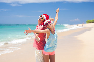 young couple in santa hats laughing on tropical beach. new year