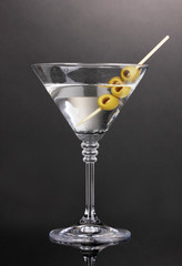 Martini glass and olives on grey background