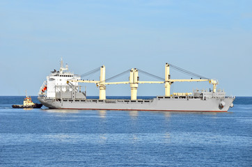 Tugboat assisting bulk cargo ship to harbor quayside