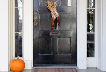 Black door with indian corn and pumpkin on doorstep