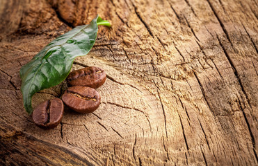 Coffee grains and green leaf on grunge wooden background