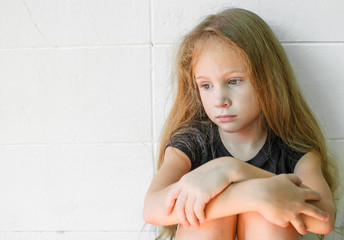 Obraz na płótnie Canvas sad little girl siedzi w pobliżu ściany