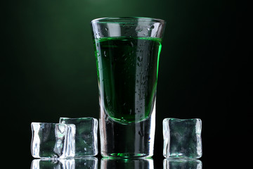 glass of absinthe and ice on green background.