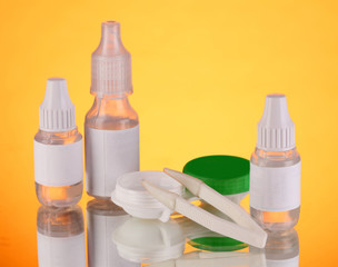 Eye drops and lenses on orange background