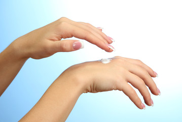 Beautiful woman hands with cream, on blue background