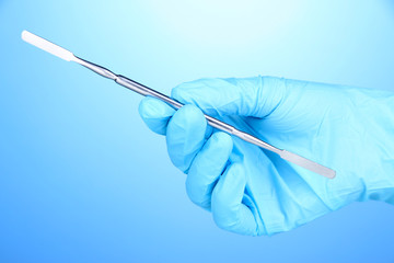 Hand in blue glove holding dental tool on blue background