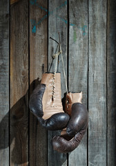 Brown old boxing gloves with a lace over old wooden wall - 47053310