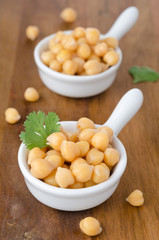 Two cups of boiled chickpeas on a wooden background