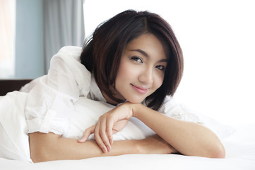 Obraz na płótnie Canvas Szczęśliwa młoda kobieta azjatyckich leżącego na łóżku z uśmiechniętą twarz