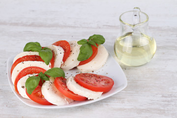Tomato and mozzarella with basil leaves on a white plate