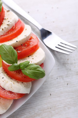 Tomato and mozzarella with basil leaves on a white plate