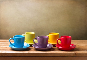 Colorful coffee cups on wooden table over grunge background