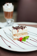 Tiramisu cake with a cherry and mint on white plate on table in 