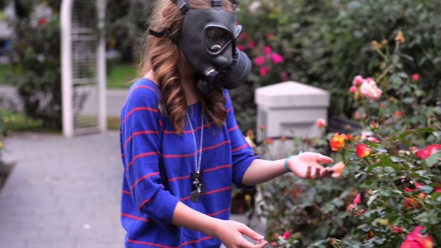 girl in gas masks smells flowers