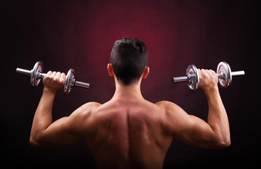 Muscular young man lifting weights from back against black backg