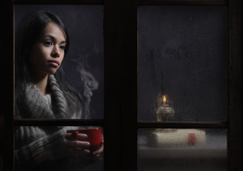 Woman behind wet window with a cup of coffee or tea