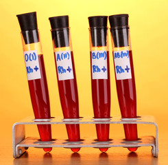 Test-tubes with blood on wooden table on yellow background