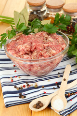 Bowl of raw ground meat with spices on wooden table