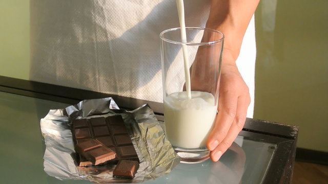 Pouring milk in a glass with chocolate on the table