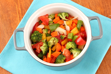 Vegetable stew in gray pot on color napkin on wooden background