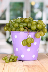 Ripe green grapes in pail on wooden table on window background